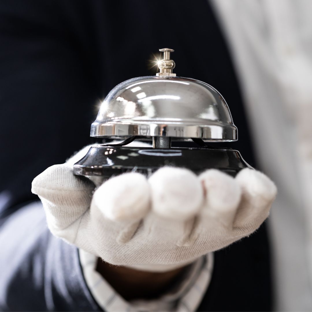 White-gloved hand of a luxury concierge presenting a polished service bell, symbolising the high-touch standards of concierge services.
